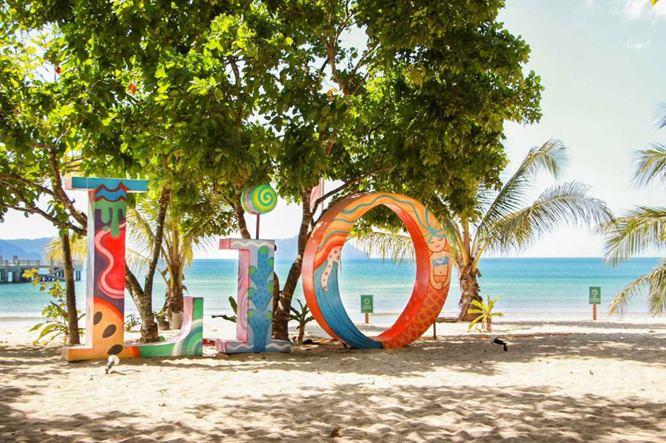 Colorful LIO letters on the sand under shade trees at Lio Beach