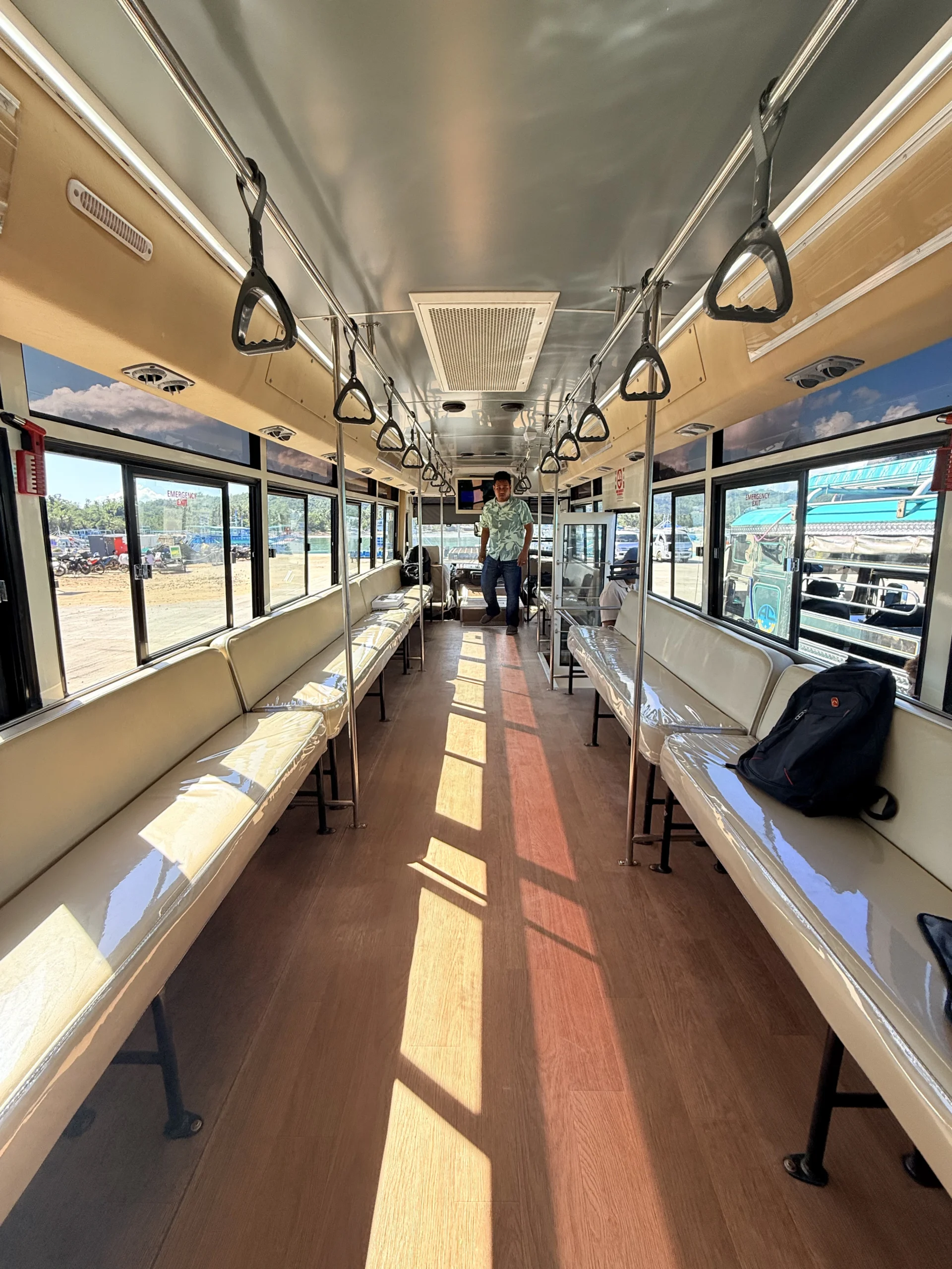 Inside the air-conditioned bus: cream bench seats along both sides, grab handles and a ceiling vent